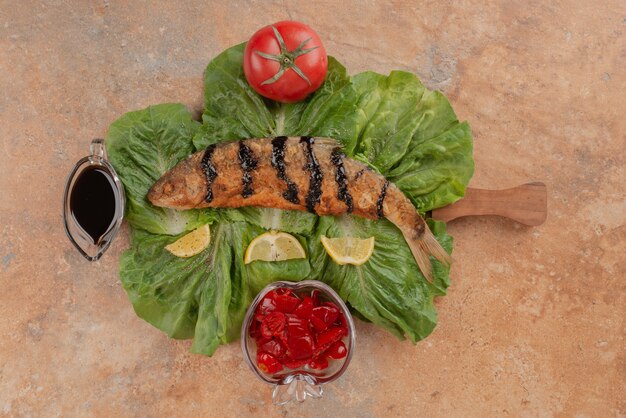 Poisson frit sur laitue avec tranches de citron, cornichons et sauce à la grenade.