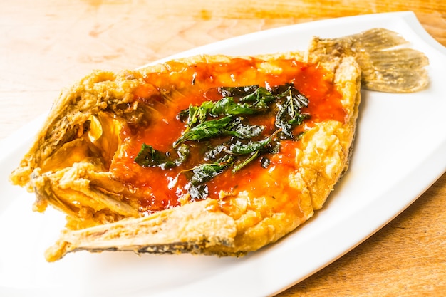 Poissons de bar frits dans une assiette blanche avec une sauce épicée et sucrée