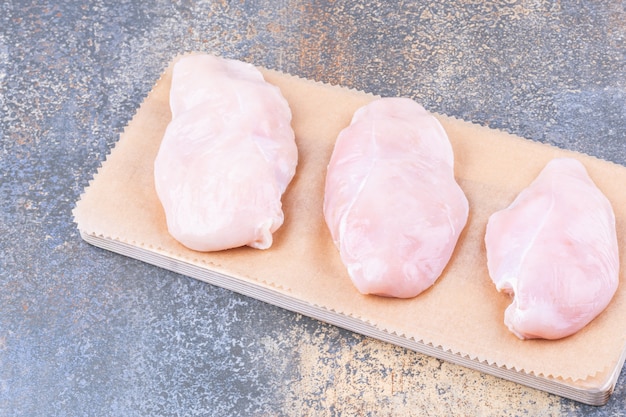 Photo gratuite poitrine de poulet sur une planche, sur la table en marbre.