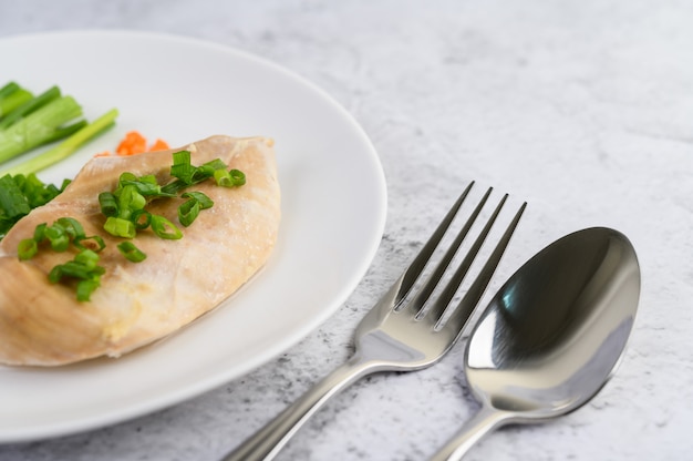 Poitrine de poulet à la vapeur sur une plaque blanche avec des oignons de printemps et des carottes hachées