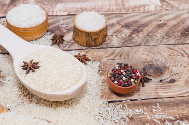 Poivre noir frais et anis étoilé avec riz cru sur une table en bois