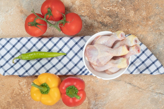 Poivrons aux tomates et cuisses de poulet cru sur nappe