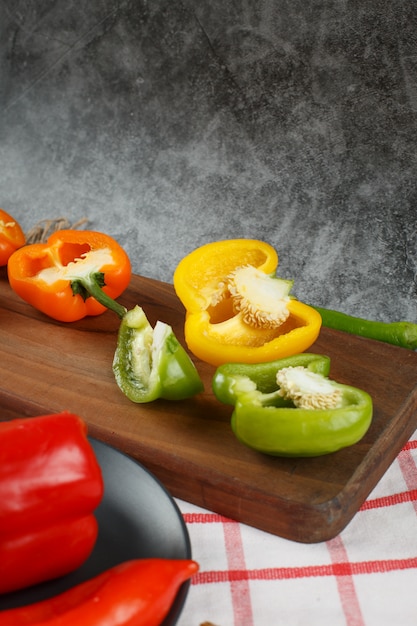 Poivrons colorés coupés à moitié sur une planche de bois.