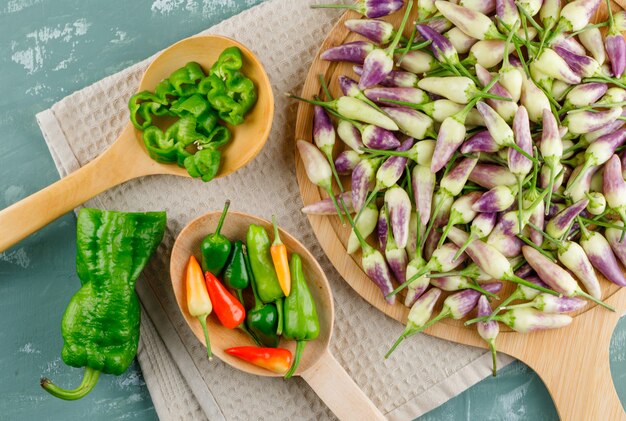 Poivrons dans des cuillères en bois avec une serviette de cuisine à plat sur du plâtre et une planche à découper