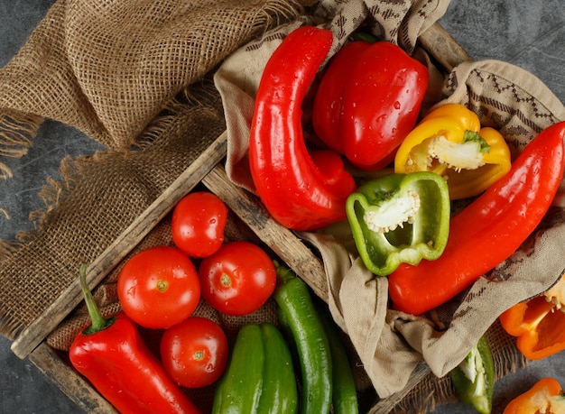 Poivrons, piments et tomates dans un plateau rustique. Vue de dessus.