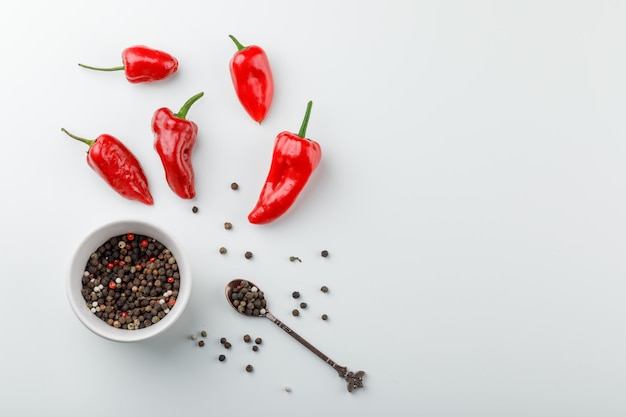 Poivrons rouges avec des grains de poivre en cuillère et vue de dessus de plaque sur un mur blanc