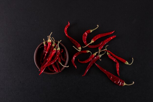 poivrons rouges et piments rouges dans un bol en bois sur une surface noire