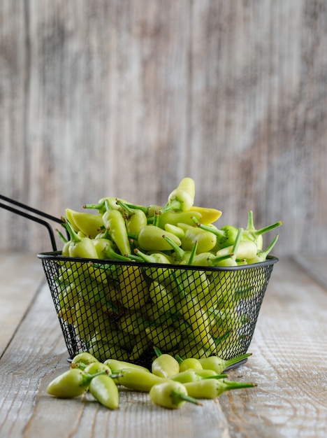 Photo gratuite poivrons verts dans une passoire en bois, vue latérale.