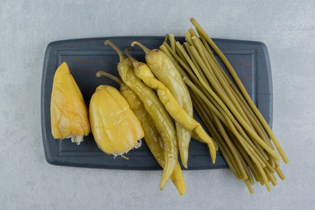 Poivrons et verts marinés sur planche sombre.