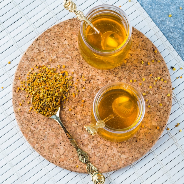 Photo gratuite pollen d'abeille à la cuillère avec des pots de miel sur des dessous de verre