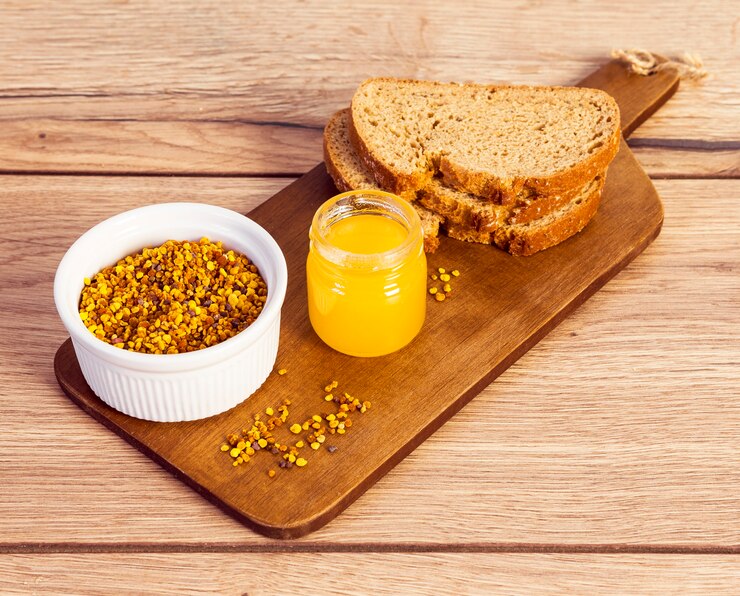 Photo gratuit pollen d'abeille avec du miel et du pain sur une planche à découper en bois sur le bureau