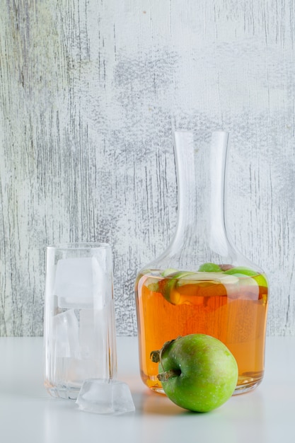 Pomme avec boisson, glaçons en verre sur blanc et grungy, vue latérale.