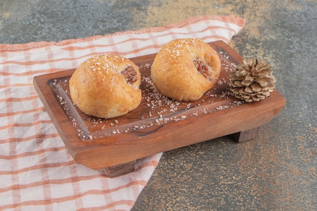 Pomme de pin à côté de deux délicieux biscuits sur planche de bois sur marbre.