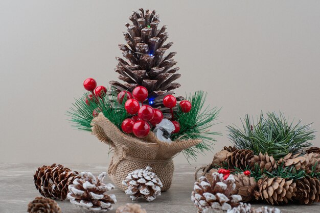 Pomme de pin décorée de baies de houx et de branches sur table en marbre.