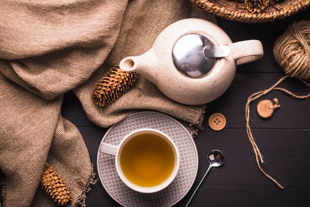 Pomme de pin; thé; théière; sac; bouton et pelote de laine sur table
