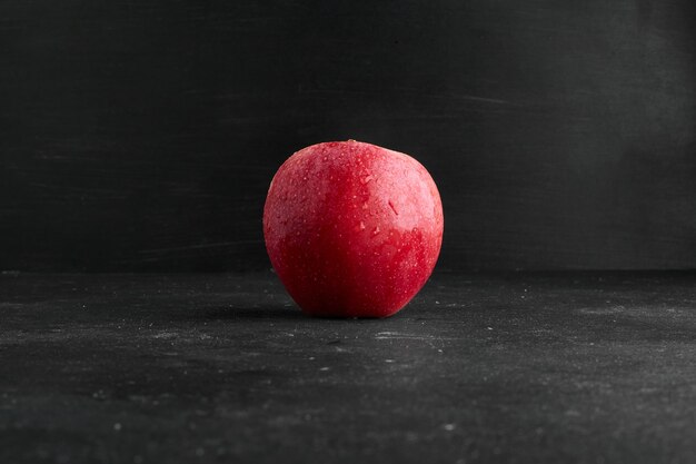 Une pomme rouge isolée sur une surface noire.