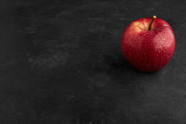 Une pomme rouge isolée sur une surface noire.