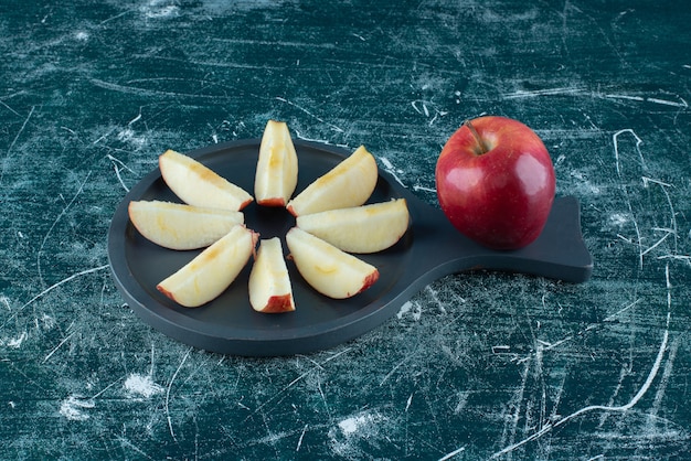 Pomme rouge tranchée et entière sur planche de bois sombre.