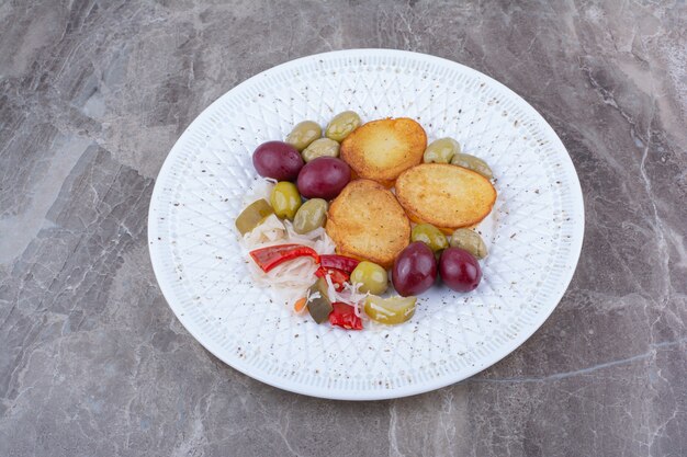 Pomme de terre rôtie et divers cornichons sur plaque blanche.