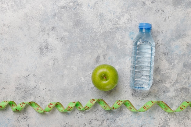 Pomme verte fraîche, ruban à mesurer et bouteille d'eau fraîche sur béton gris