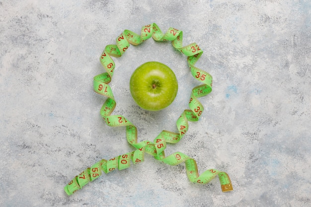 Photo gratuite pomme verte fraîche, ruban à mesurer et bouteille d'eau fraîche sur béton gris