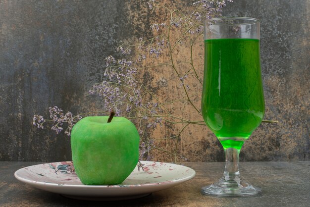 Une pomme verte fraîche avec un verre d'eau verte sur une assiette sombre.