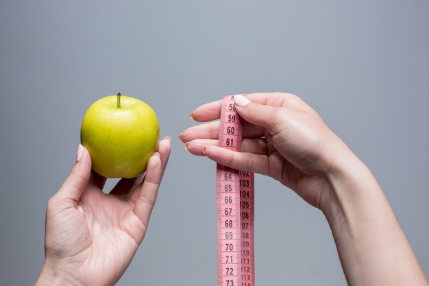 Pomme verte et ruban à mesurer en mains féminines sur mur gris