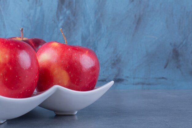 Pommes biologiques dans une assiette sur table en marbre.