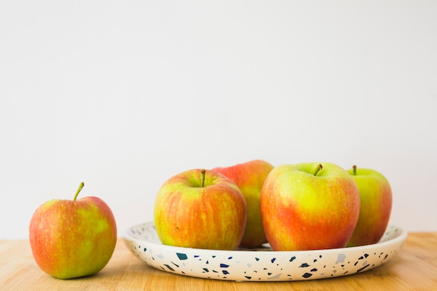 Pommes biologiques fraîches sur plaque sur la table en bois contre blanc