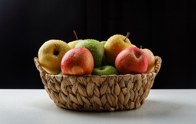 Pommes colorées dans un panier en osier sur noir et blanc