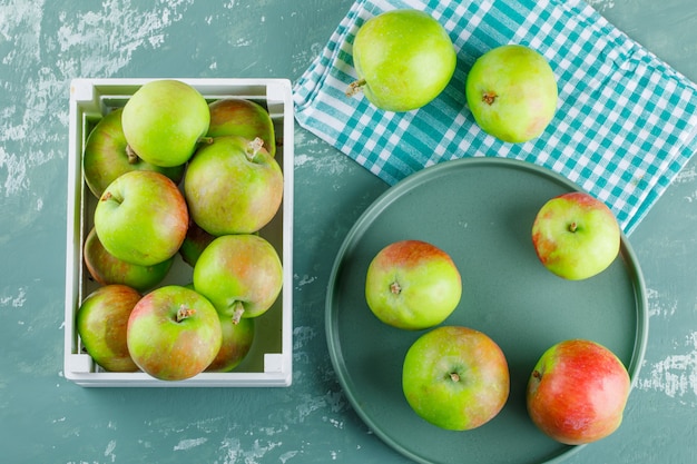 Pommes dans une boîte en bois et plateau sur fond de plâtre et de tissu de pique-nique. pose à plat.