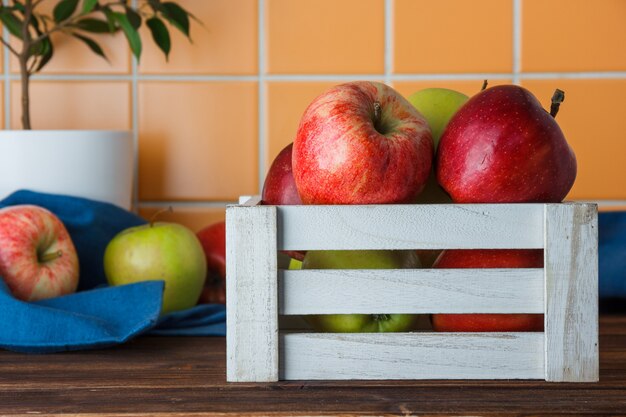 Pommes dans une vue de côté de boîte en bois blanc sur un fond de carreaux en bois et orange