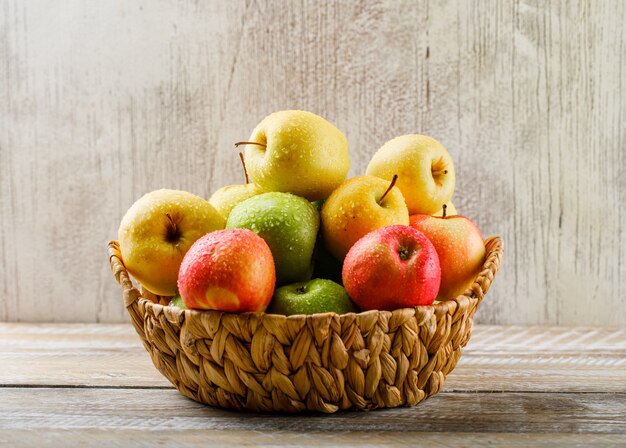 Pommes avec gouttes dans un panier en osier sur bois clair et grunge