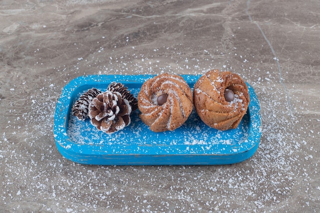 Photo gratuite pommes de pin et biscuits sur un plateau bleu sur une surface en marbre