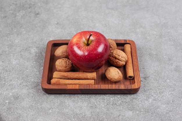 Pommes rouges, noix et bâtons de cannelle sur plaque en bois