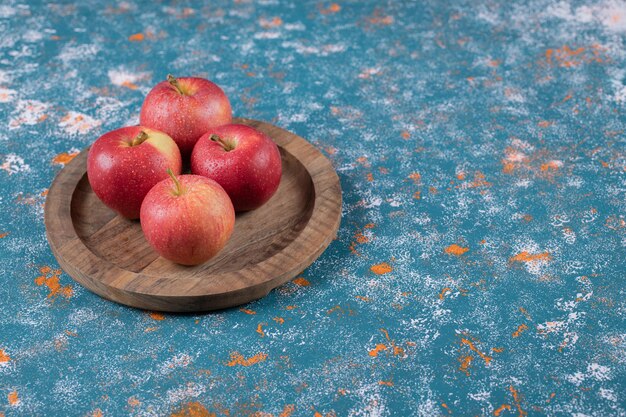 Pommes rouges sur plateau en bois sur bleu.