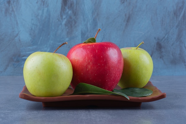 Pommes savoureuses avec des feuilles sur une plaque en bois sur la surface sombre