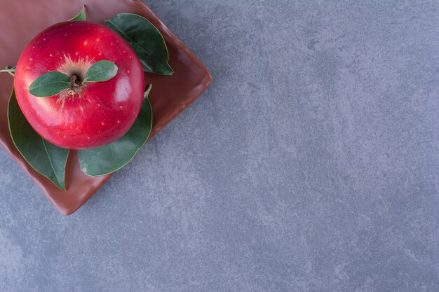 Pommes savoureuses avec des feuilles sur une plaque en bois sur une table en marbre.