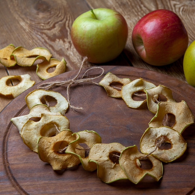 Pommes séchées sur une planche à découper ronde et pommes fraîches sur une table en bois