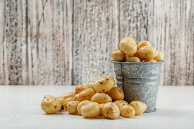 Pommes de terre dans un mini seau vue latérale sur un mur en bois blanc et grungy