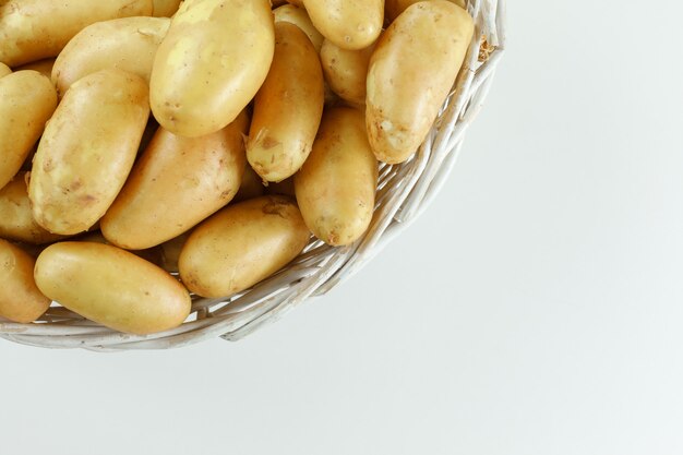 Pommes de terre dans un panier en osier sur tableau blanc, mise à plat.