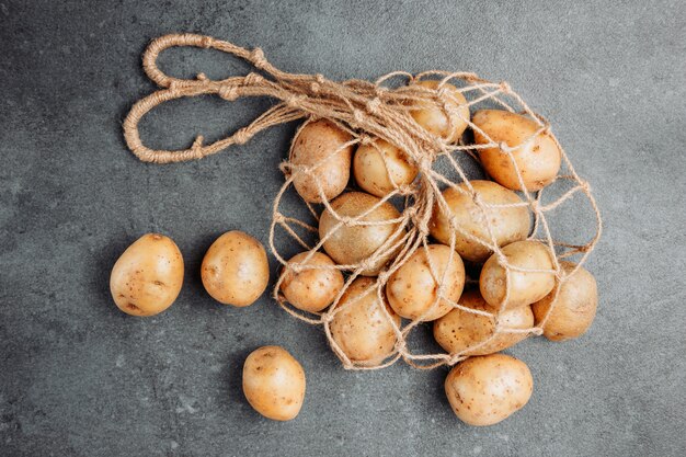 Pommes de terre dans un sac en filet sur un fond texturé sombre. mise à plat.