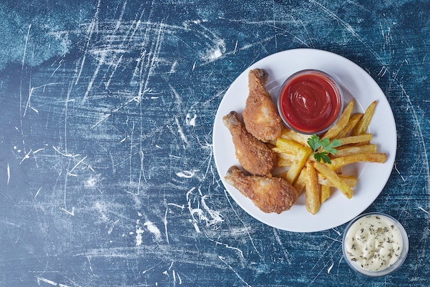 Pommes de terre frites avec cuisses de poulet et sauces.