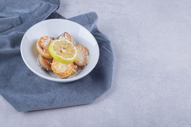 Pommes de terre frites garnies de fromage râpé et de citron sur une assiette blanche.