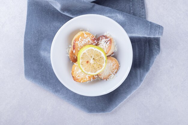 Pommes de terre frites garnies de fromage râpé et de citron sur une assiette blanche.