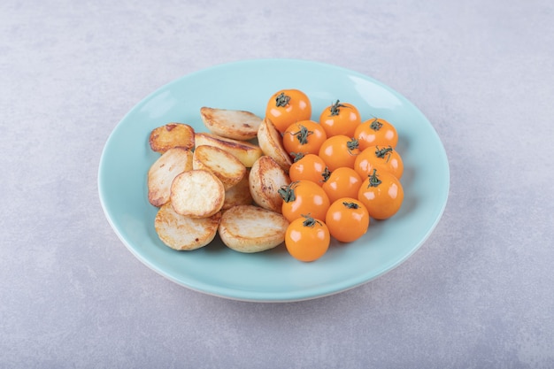 Pommes de terre frites et tomates sur plaque bleue.