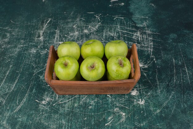 Pommes vertes dans une boîte en bois sur une surface en marbre.