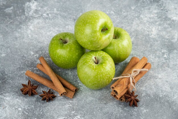 Pommes vertes entières et bâtons de cannelle sur table en marbre.