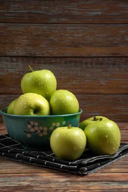 Pommes vertes fraîches avec des gouttes d'eau sur eux dans un bol bleu