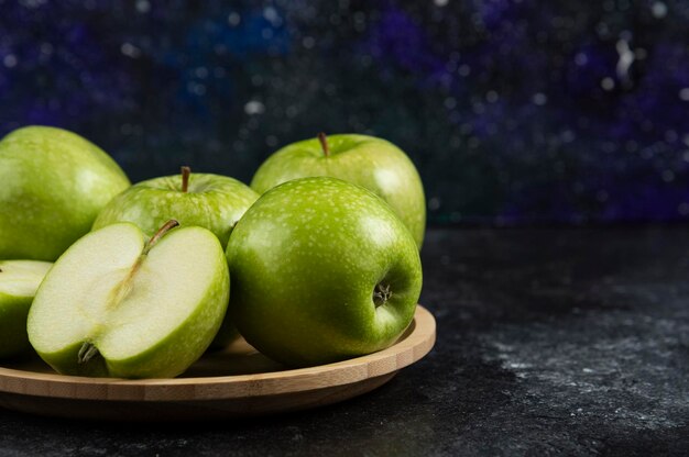 Pommes vertes mûres entières et tranchées sur une assiette en bois.